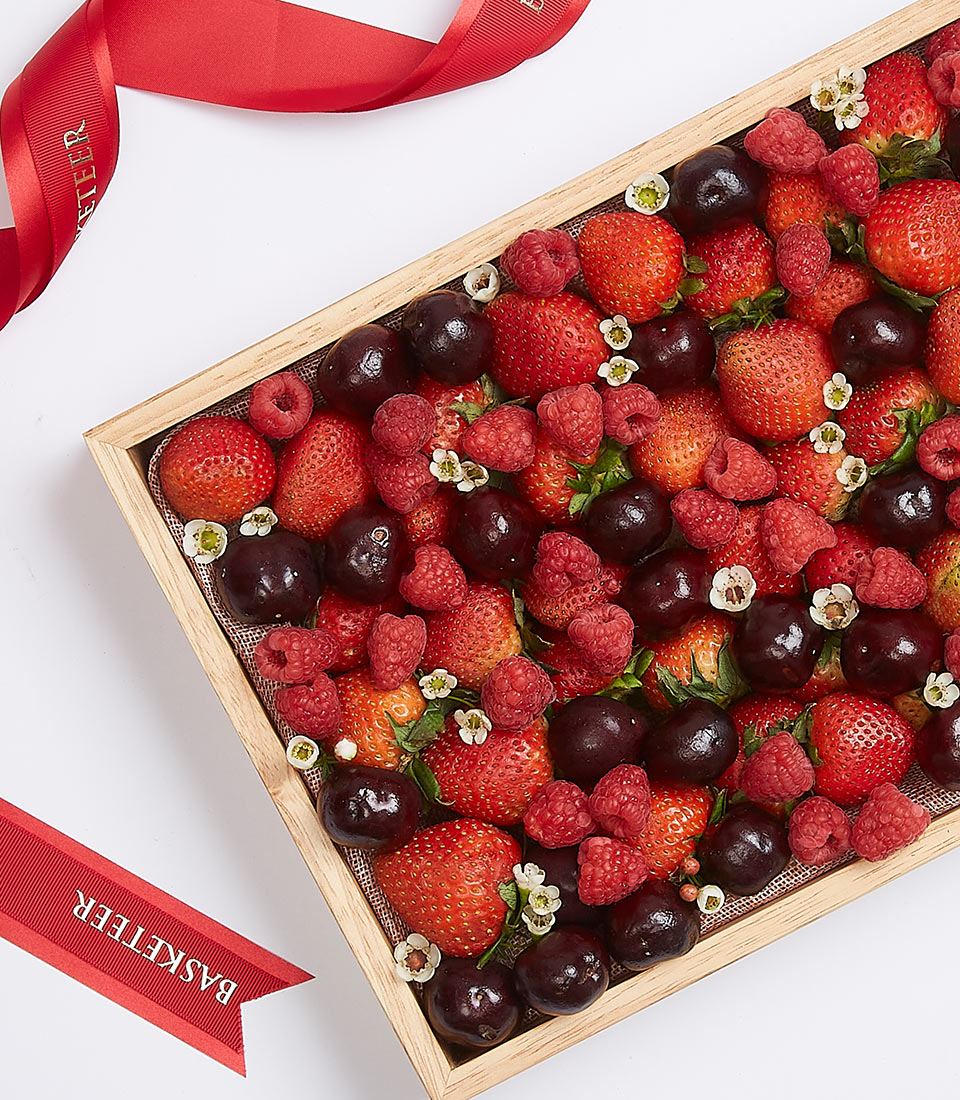 Mixed berry gift box with strawberries, cherries, and raspberries in wooden tray with ribbon