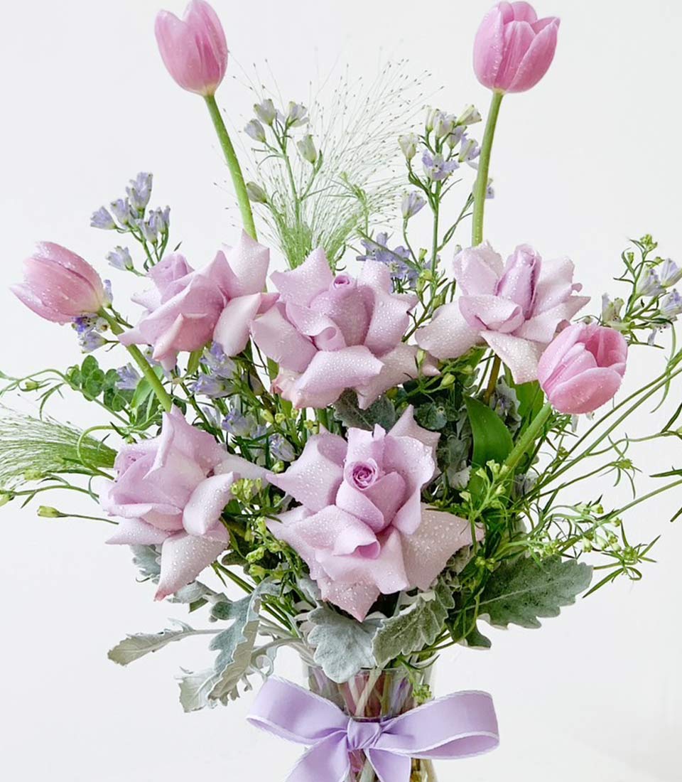 Lavender rose bouquet with pink tulips and purple flowers in glass vase with ribbon