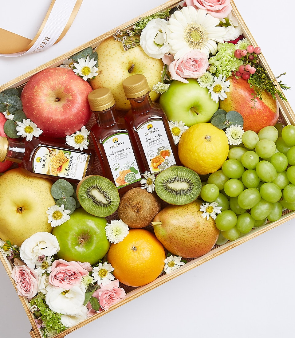 Wooden gift box filled with fresh apples, pears, kiwis, citrus fruits, grapes, honey bottles and white and pink roses