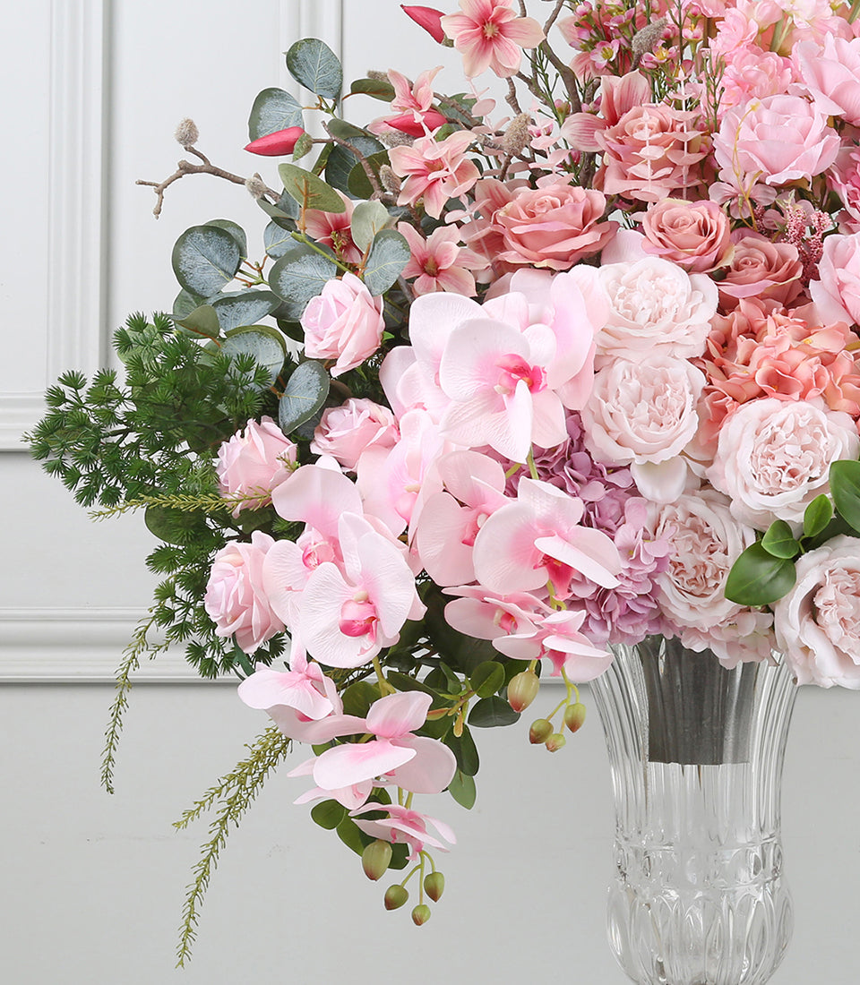 Elegant pink floral arrangement with orchids and roses in clear glass vase, lush with eucalyptus greenery