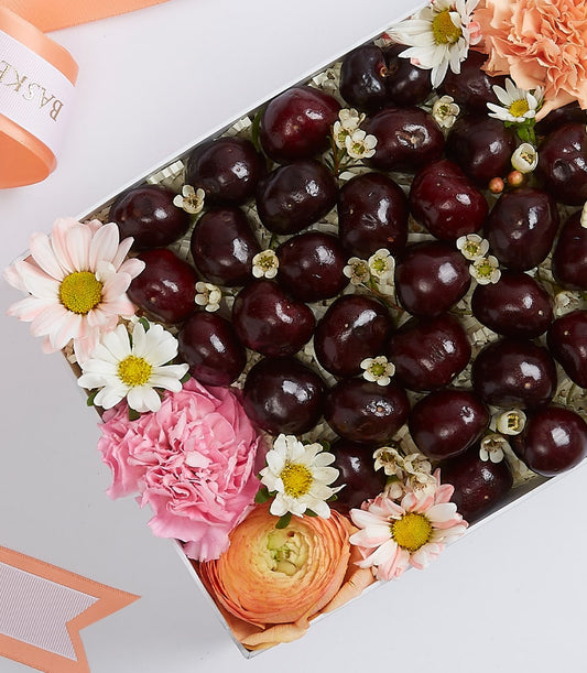Fresh dark red cherries with pink carnations and white daisies in elegant white gift box