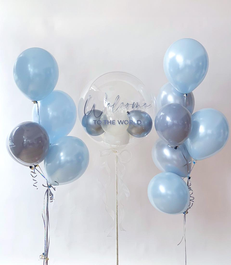 Magical welcome baby balloon bundle with light blue and grey clusters framing clear bubble inscription