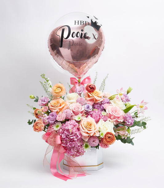 Vibrant birthday flower bouquet with pink, peach, and purple roses in white hexagonal box with personalized HBD balloon
