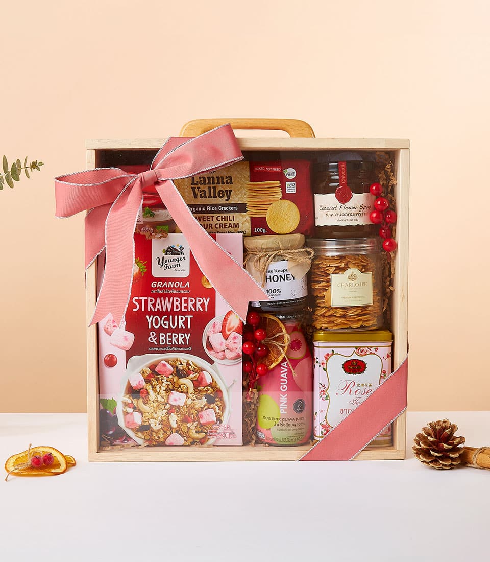 Gourmet wellness gift box with granola, organic rice crackers, honey, and coconut syrup in wooden crate with pink ribbon bow