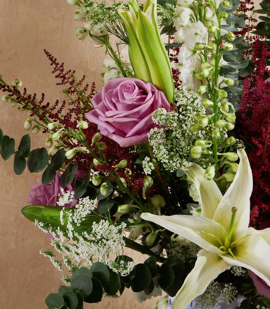 Light purple rose and white lily fresh flower vase arrangement with eucalyptus foliage