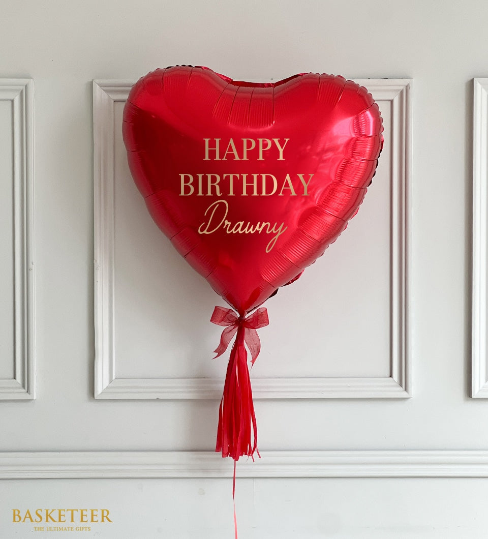 Red heart-shaped foil balloon with gold Happy Birthday text and personalized name, tied with red ribbon tassel