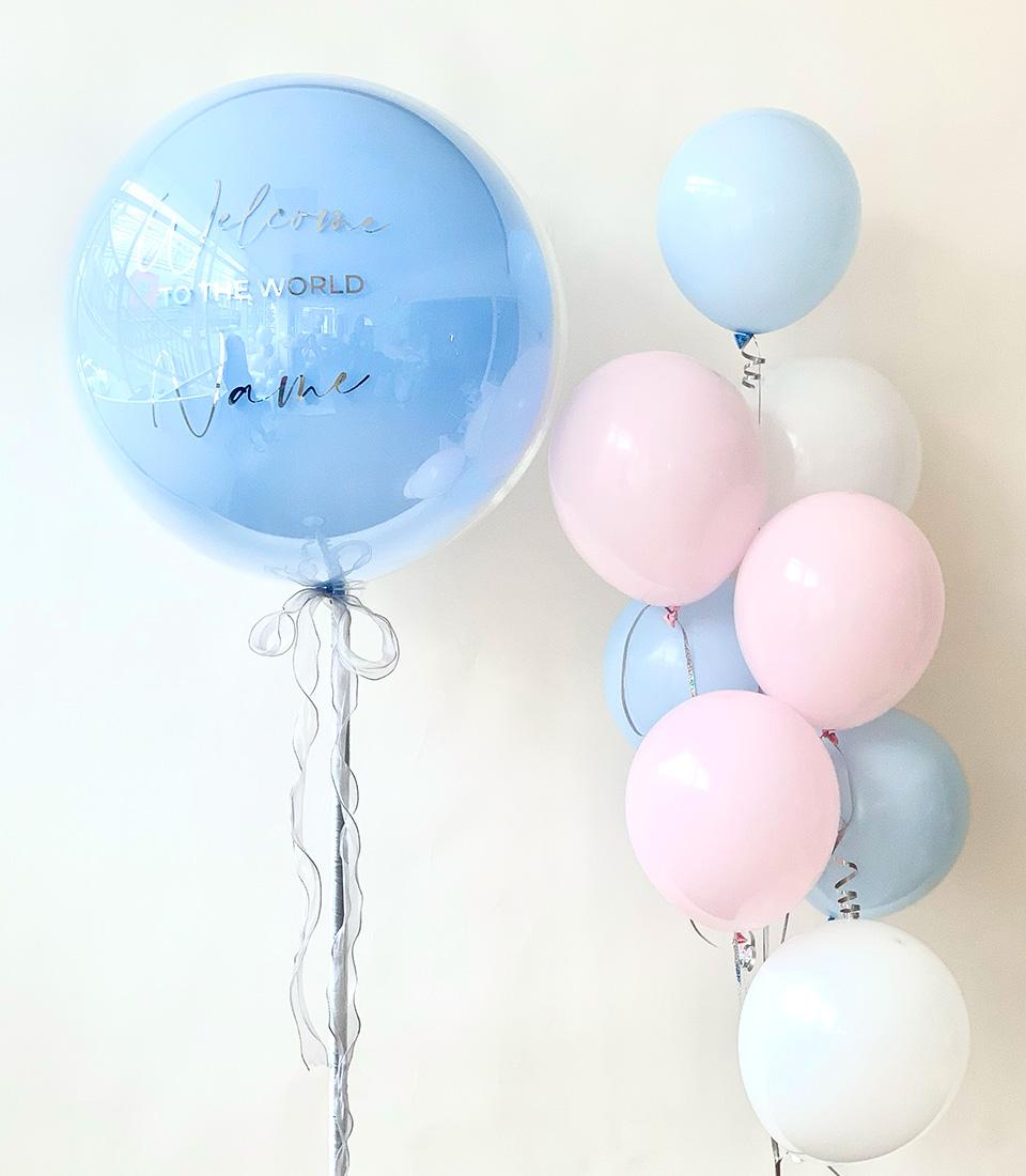 Pastel pink, blue and white balloon bundle with personalised welcome message and silver ribbons for newborn celebration