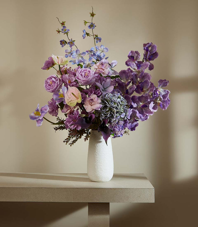 Lush purple and lavender artificial flower arrangement with orchids and roses in white textured vase