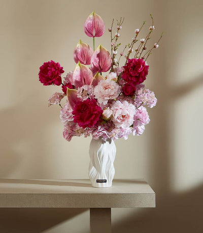 Pink and fuchsia artificial floral arrangement in textured white ceramic vase with anthuriums and peonies