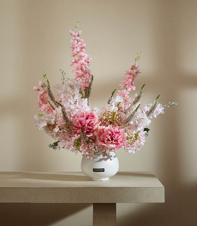 Elegant pink and white artificial flower arrangement in white ceramic vase with peonies and delphiniums