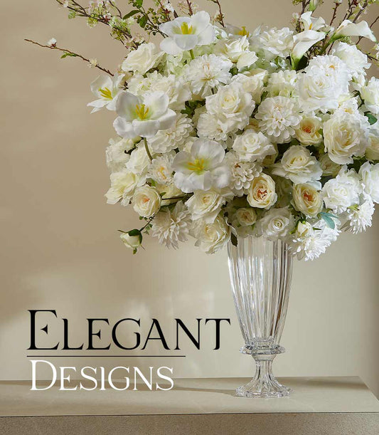 Pristine white roses, dahlias, and tulips in tall fluted crystal vase with green foliage
