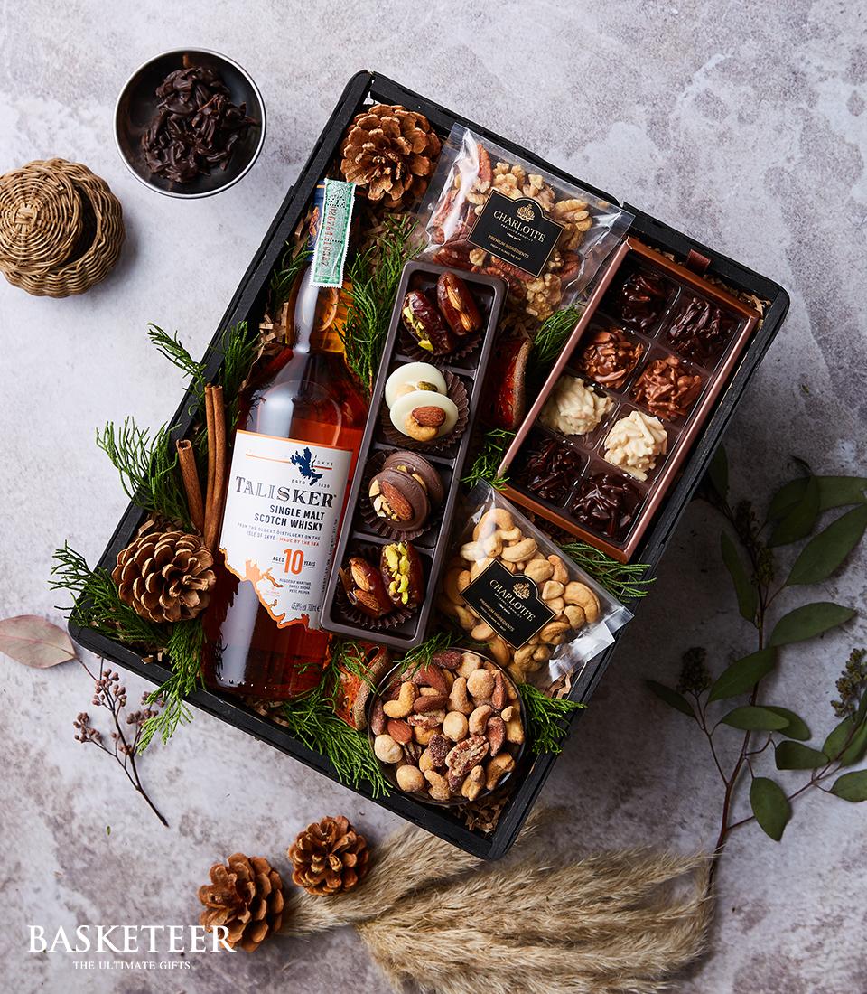 Premium Talisker Single Malt Scotch whisky gift basket with gourmet chocolates, nuts, and festive greenery in dark wooden
