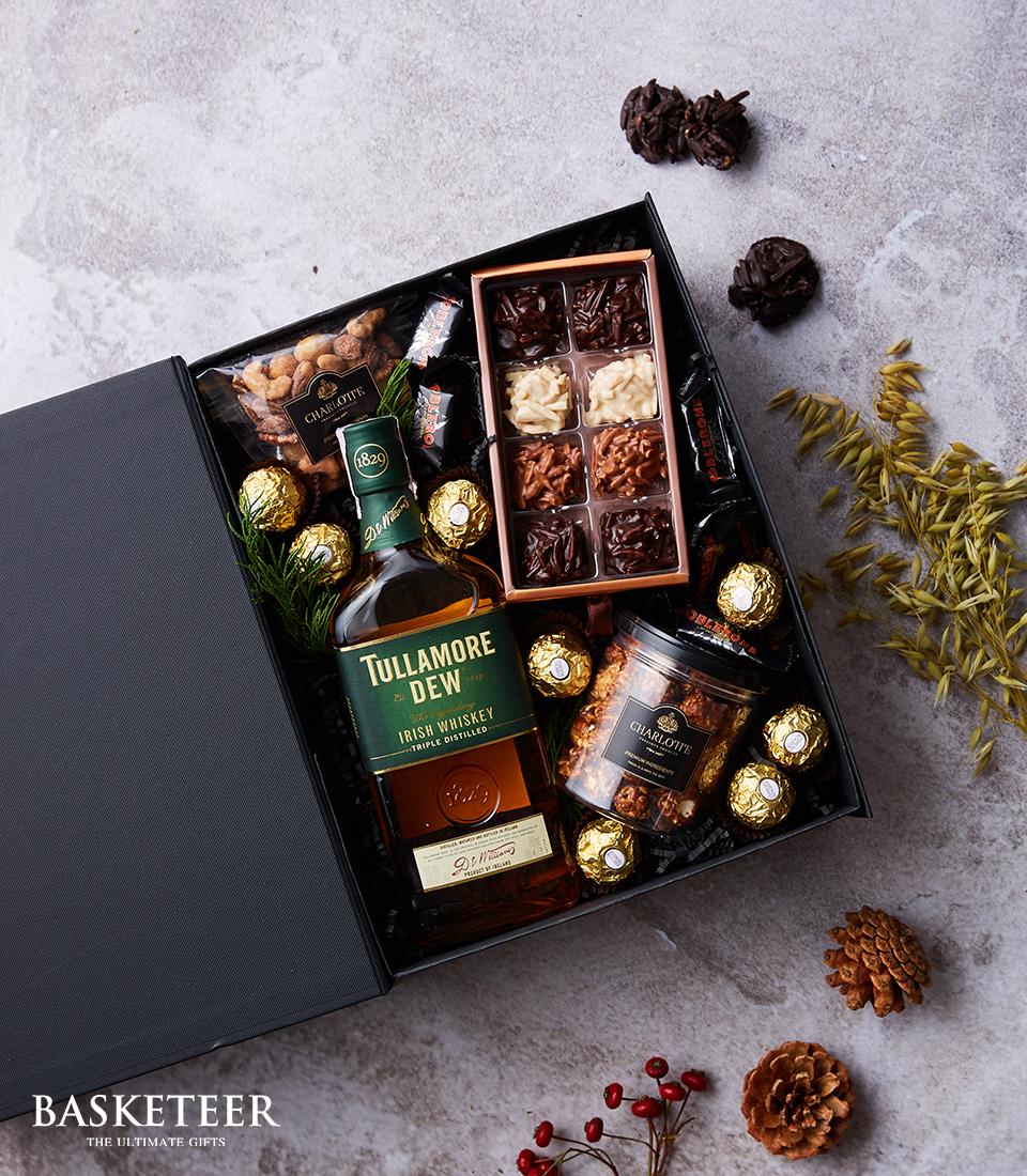 Tullamore Dew Irish Whiskey luxury gift box with gourmet nuts, assorted chocolates, and gold truffles on grey surface