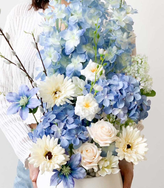 Blue and white artificial floral arrangement with hydrangeas, gerberas, and roses in white vase
