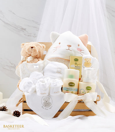 Newborn baby gift basket with brown teddy bear, white embroidered clothing, and gentle care products in wooden crate