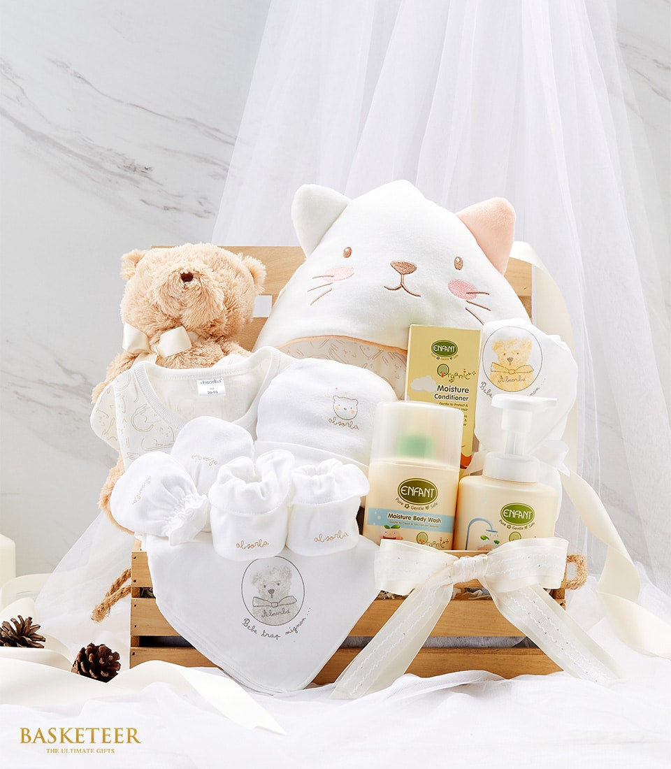 Newborn baby gift basket with brown teddy bear, white embroidered clothing, and gentle care products in wooden crate
