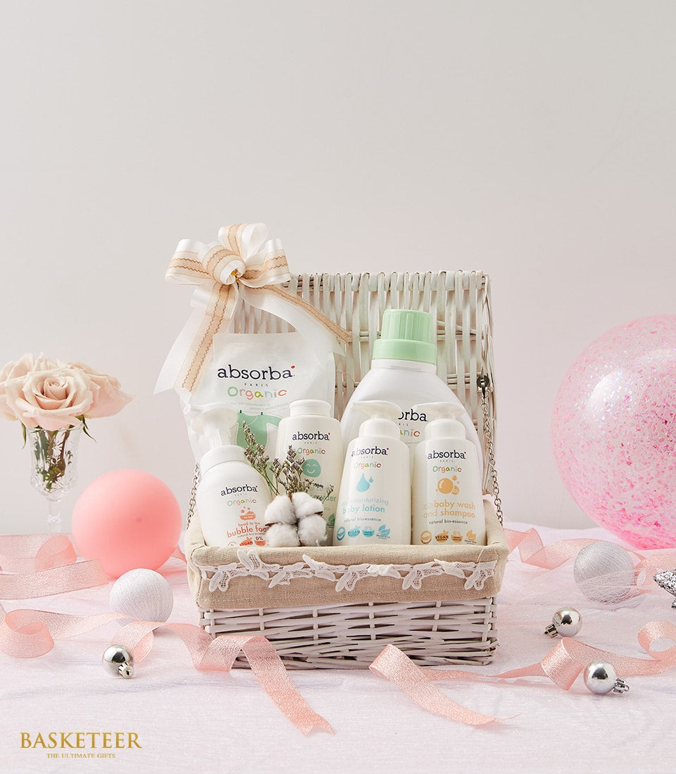 White woven baby gift basket with organic care products, pink roses, and ribbon for newborn arrival