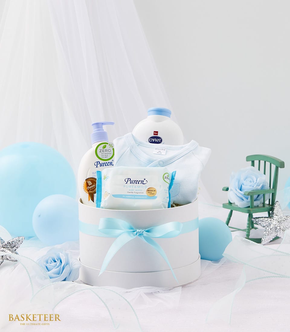 Blue newborn gift box with onesie, baby lotion, powder, and wipes, nestled in white packaging with light blue ribbon and