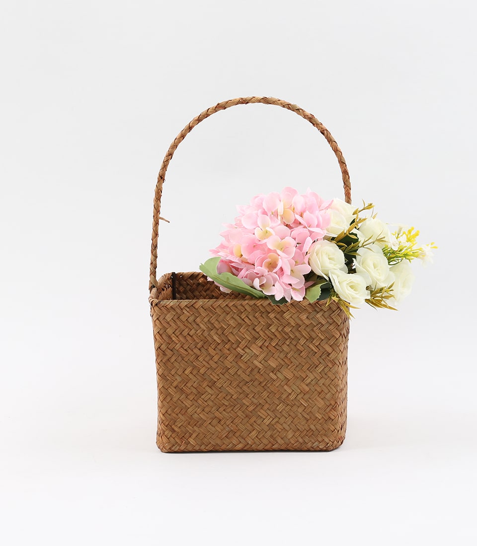 Natural woven seagrass basket with light pink hydrangeas, white roses, and green foliage arrangement