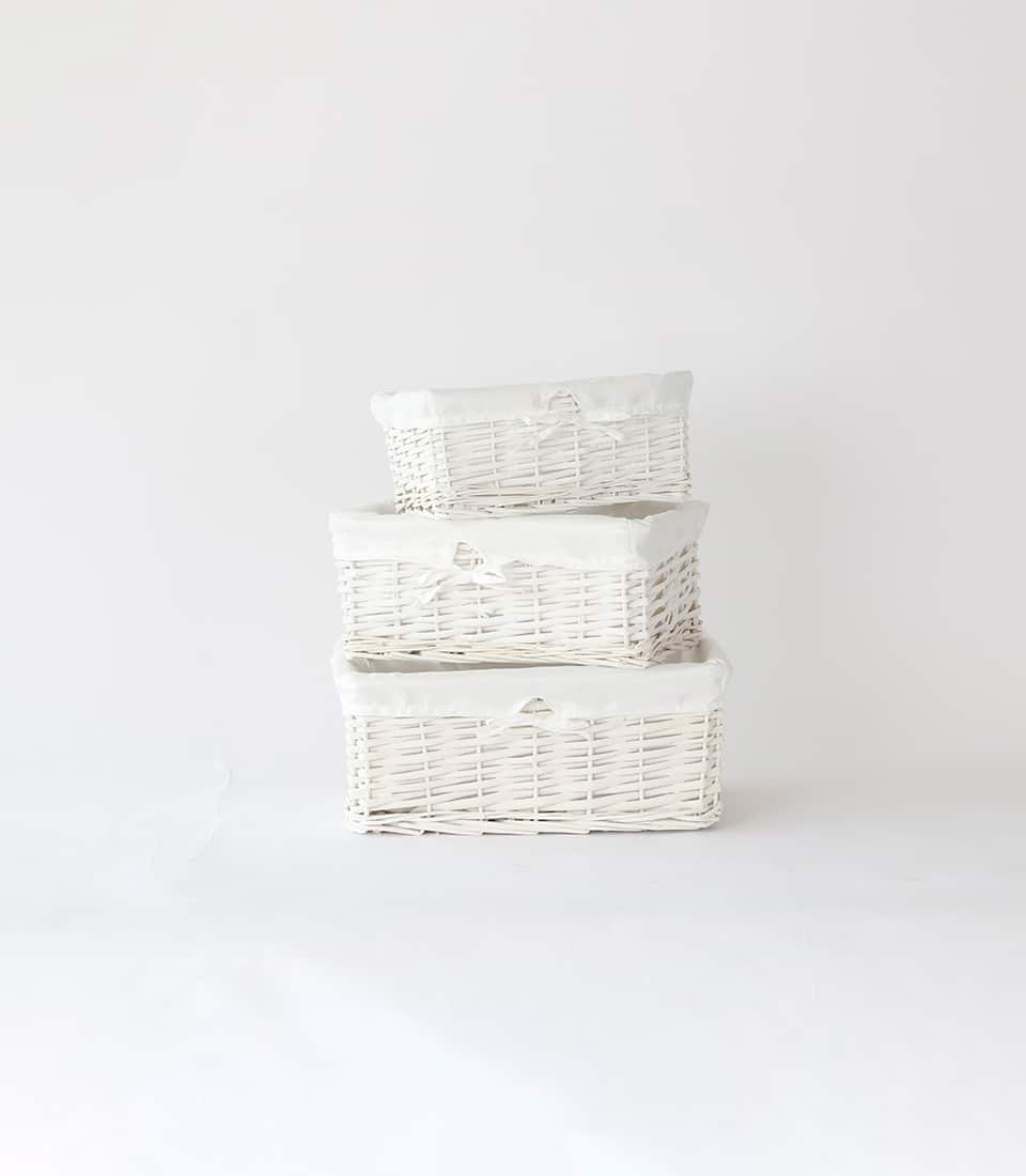 Tiered white wicker storage baskets with fabric liners and ribbon bows for luxury gift hampers