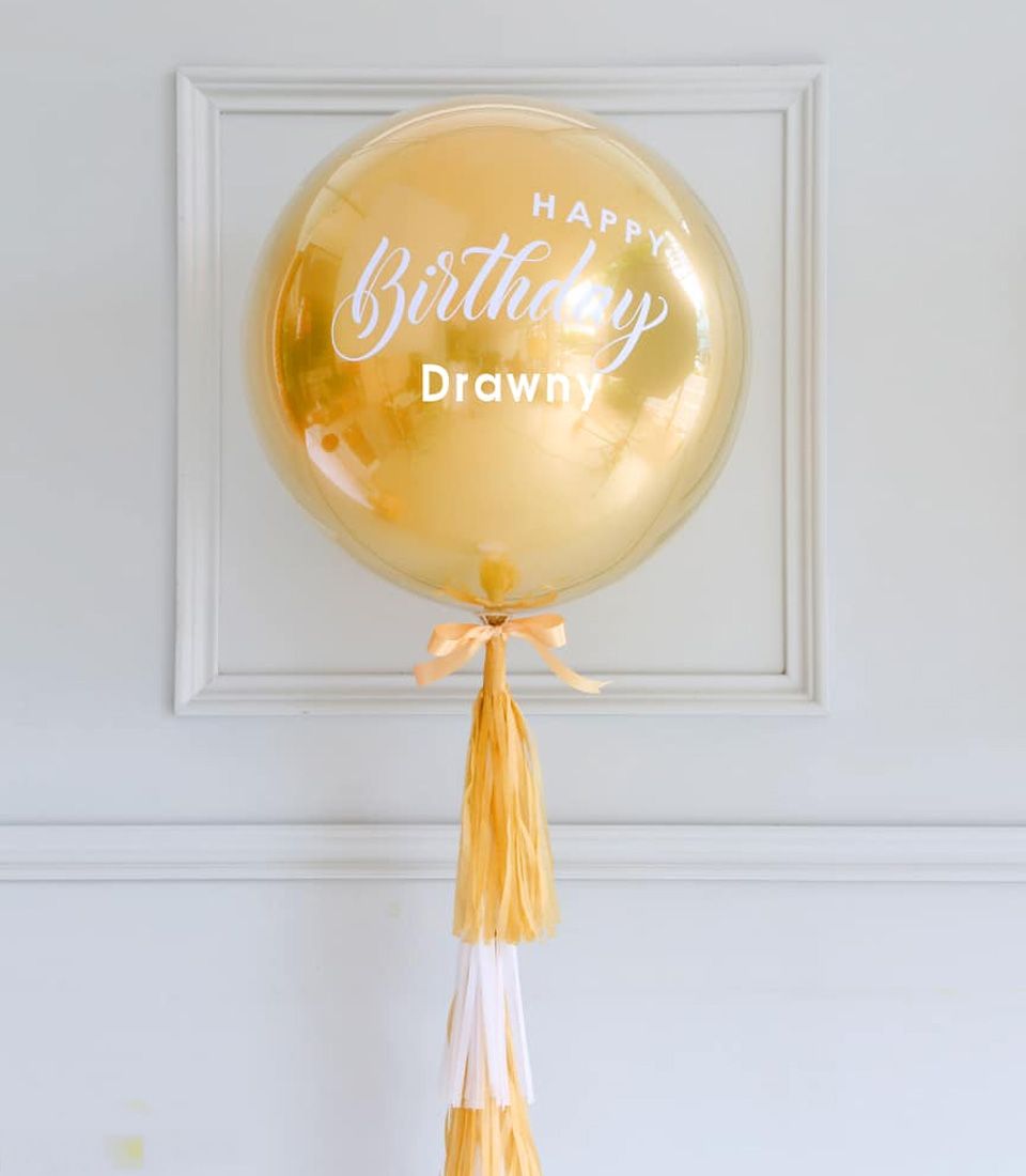 Gold Happy Birthday bubble balloon with white text and peach ribbon tassel garland