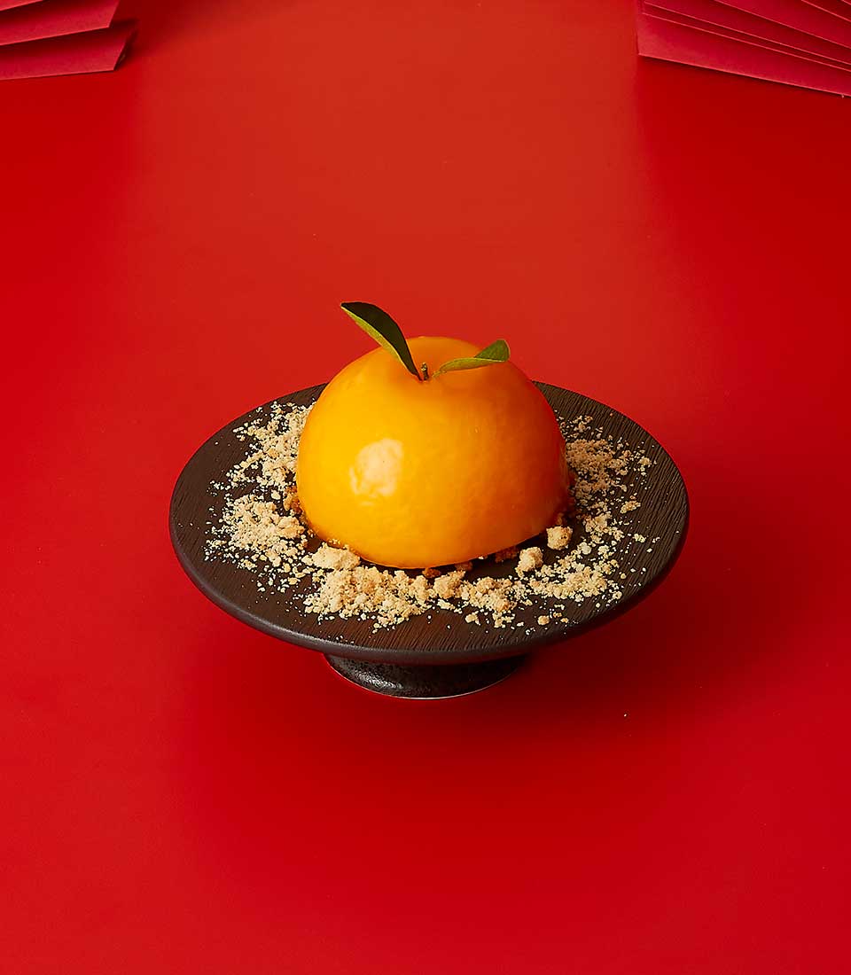 Creamy mandarin orange sphere cake with glossy finish and green leaf accent, Chinese New Year celebration dessert