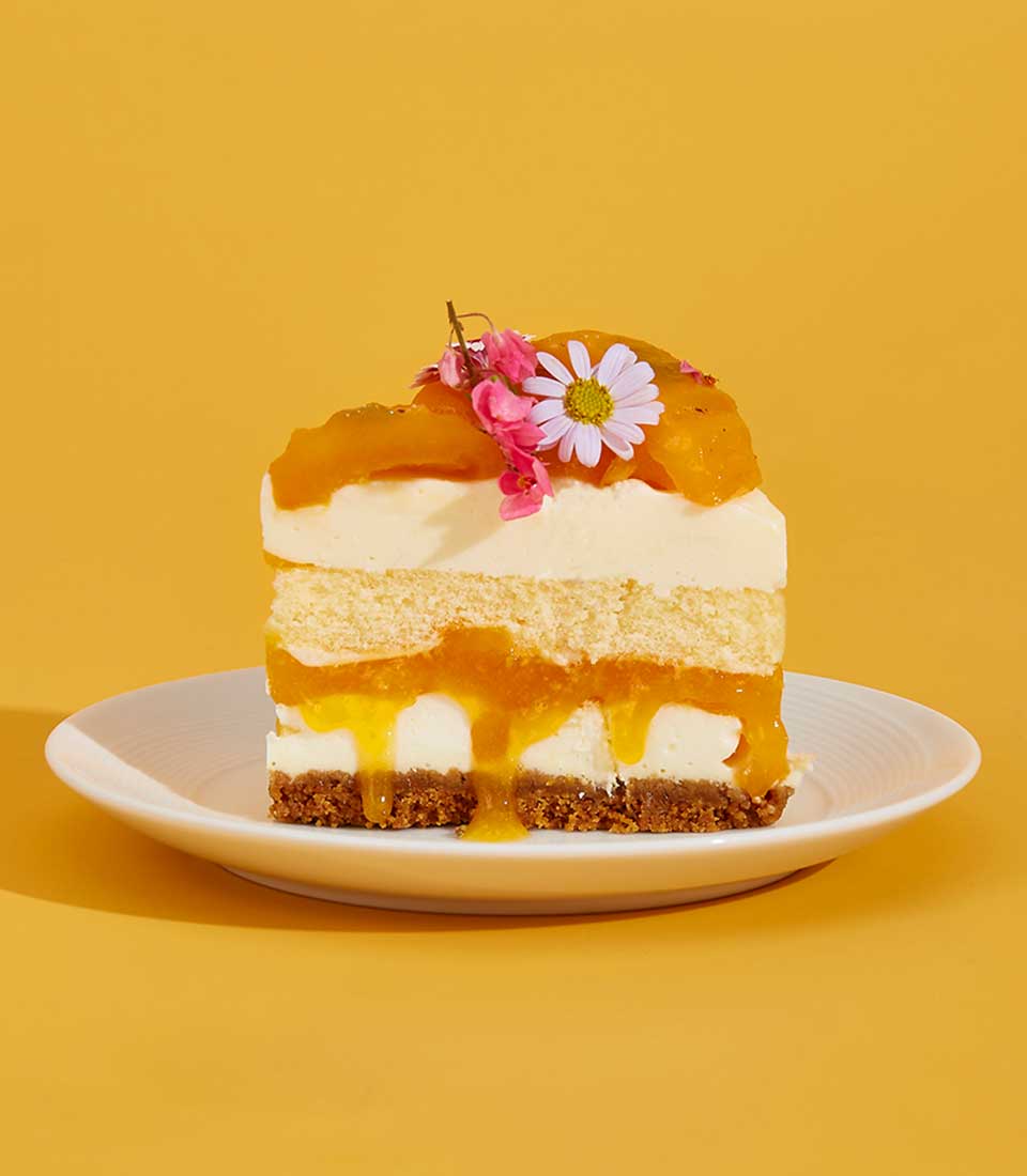 Layered mayongchid cake with white cream, yellow sponge, fresh diced mango, and edible flowers on ceramic plate