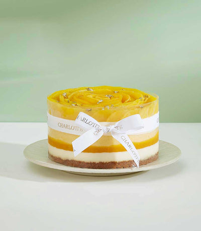 Exotic mango layer cake with creamy white mousse, mango spiral topping, and gold leaf detail, tied with Charlotte ribbon