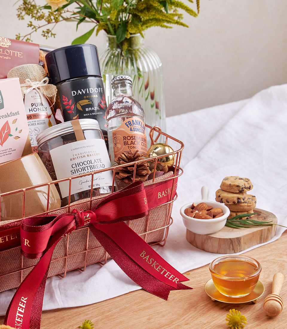 Luxury rose gold wire mesh gift basket with red ribbon bow containing gourmet coffee, artisan chocolate shortbread, honey,