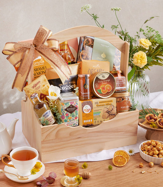 Wooden hamper filled with gourmet cookies, nuts, premium tea, organic honey and artisan pantry goods with gold ribbon