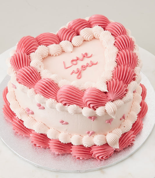 Heart-shaped vanilla cake with pink and ivory frosting, love message, and heart sprinkles for birthdays and romantic
