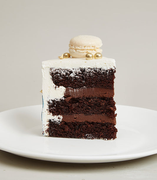 White chocolate layered birthday cake slice with dark ganache and gold macaron decoration