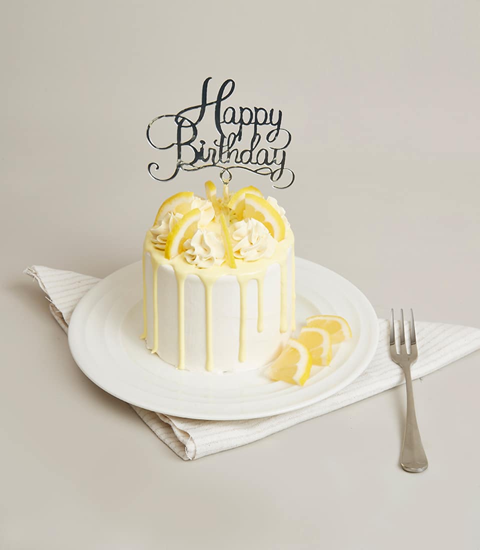 Lemon white cream mini cake with citrus drip glaze and birthday topper on ceramic plate