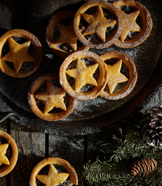 Star-shaped mince pies dusted with powdered sugar, golden pastry with festive evergreen and pinecones on rustic wood