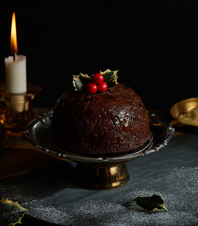 Dark traditional British Christmas pudding with holly berries and leaves on silver cake stand, festive holiday dessert