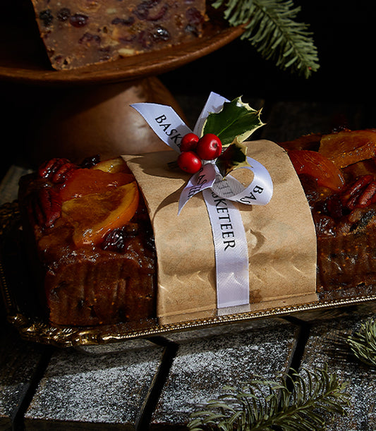 Majestic Reserve fruitcake wrapped in brown paper with white ribbon, topped with candied orange and pecans, displayed on