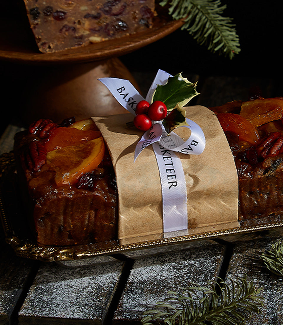 Majestic Reserve fruitcake wrapped in brown paper with white ribbon, topped with candied orange and pecans, displayed on