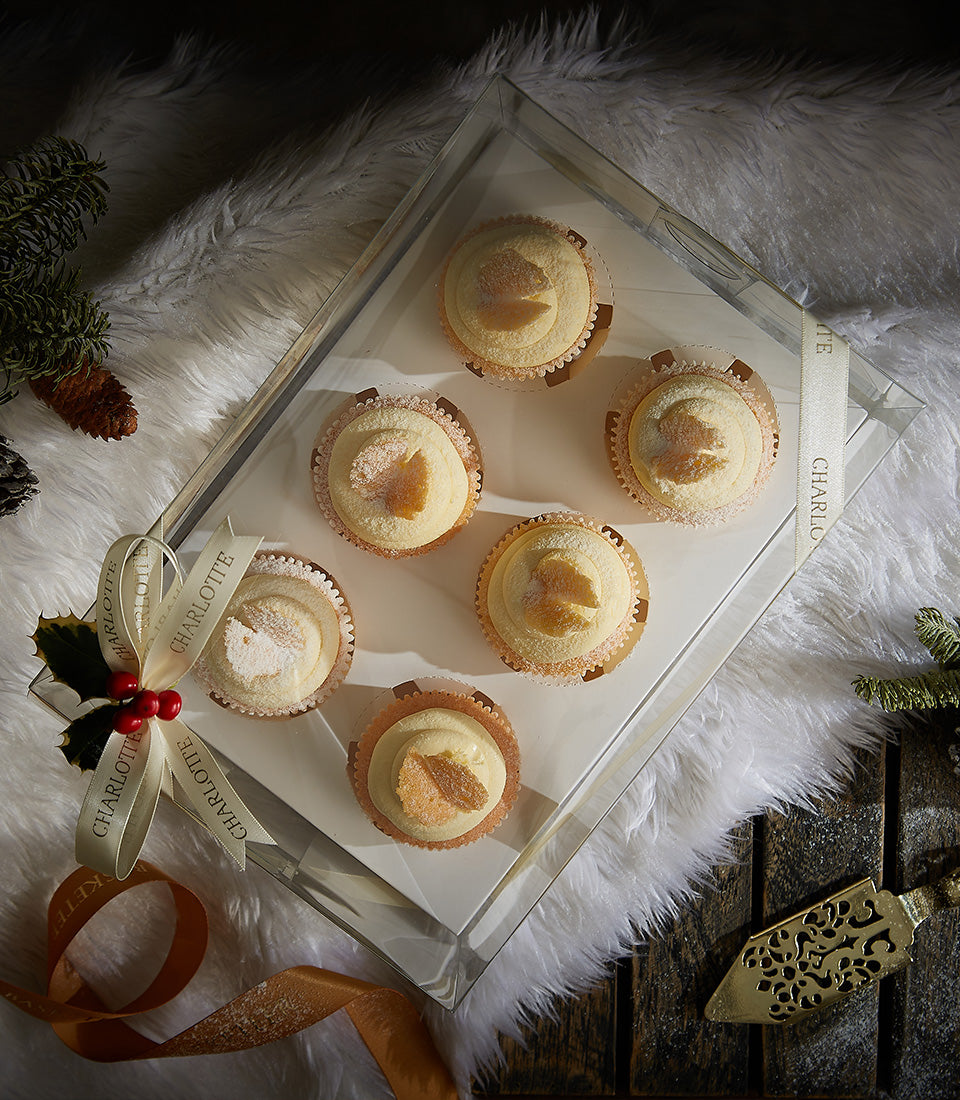 Six vanilla buttercream cupcakes with candied ginger and powdered sugar in festive gift box with holly ribbon