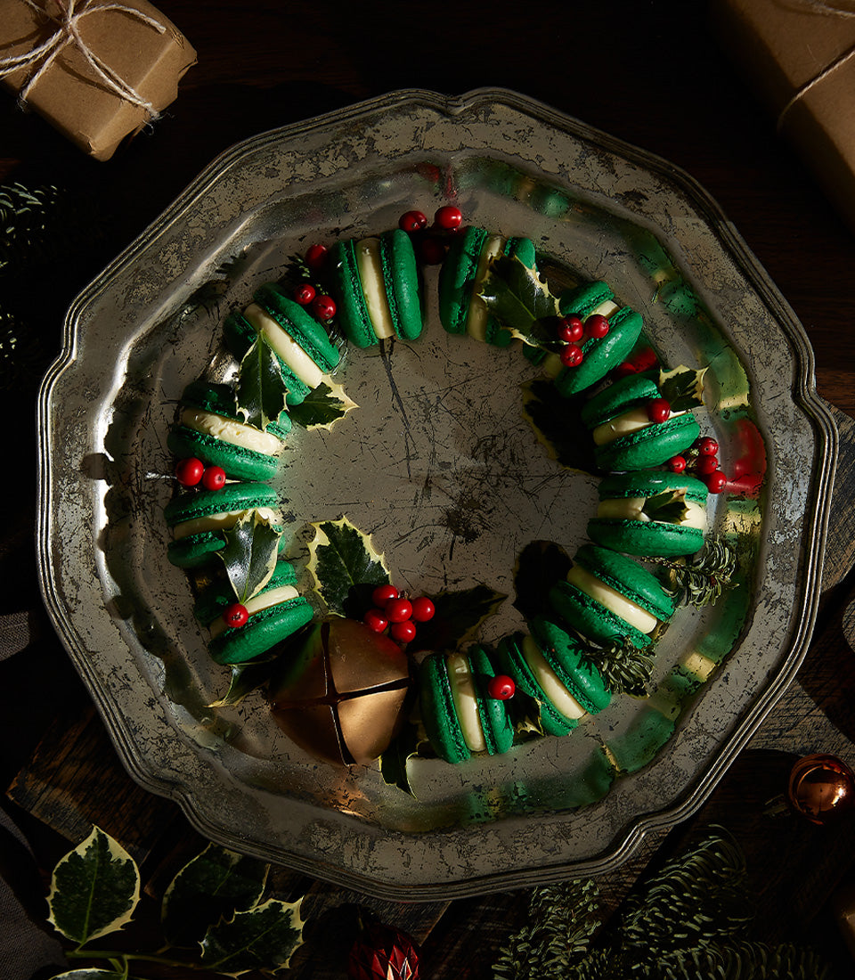 Green macaron Christmas wreath with brandy butter cream filling and holly berries on silver platter