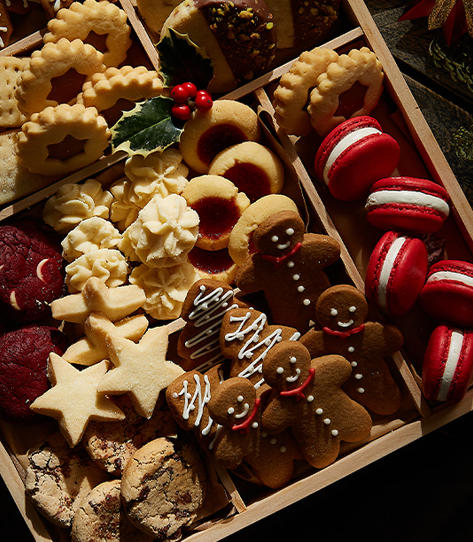 Assorted Christmas cookies and treats in wooden compartments with gingerbread, shortbread, and macarons