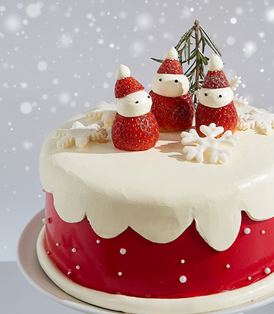 Red and white Christmas cake with strawberry Santa figures and snowflake decorations on white cake stand