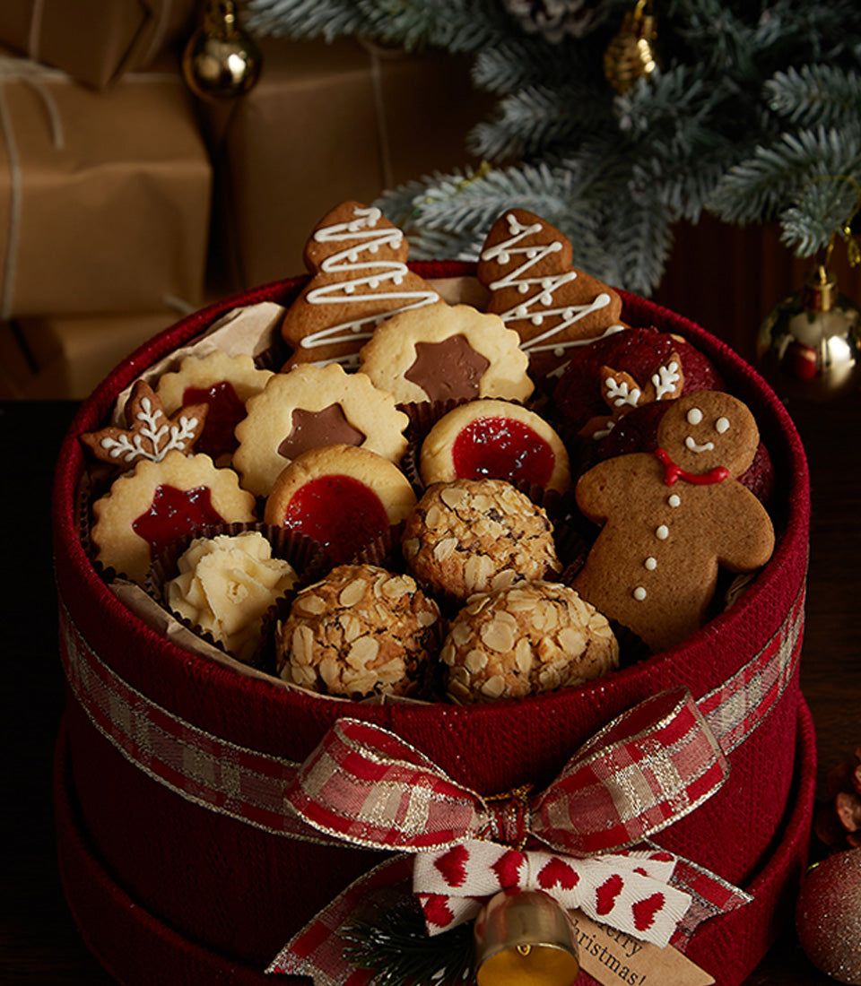 Festive red round gift box with assorted Christmas cookies, gingerbread men, and shortbread tied with plaid ribbon