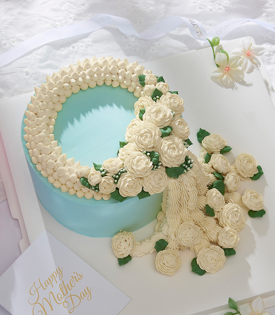 Light blue Mother's Day cake with cascading cream roses and green leaves on white board