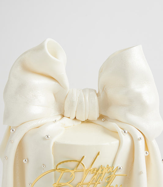 White pearl bow fondant birthday cake with silver edible pearls and gold happy birthday topper