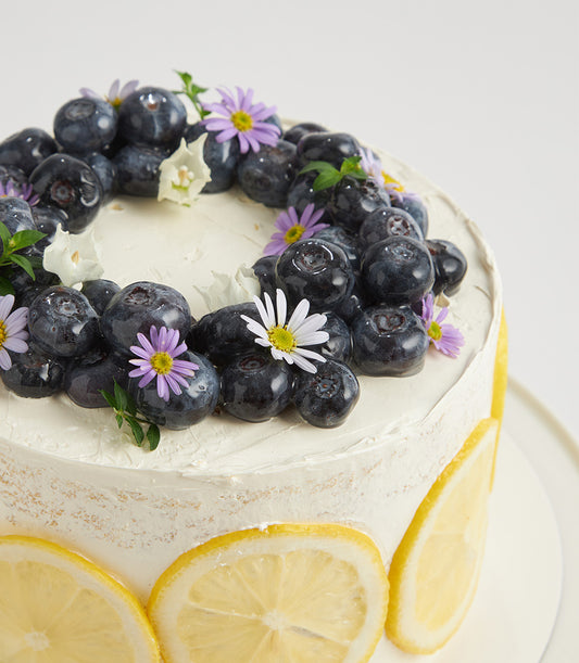 Lemon zest buttercream layer cake with fresh blueberries, white flowers, and candied lemon slices