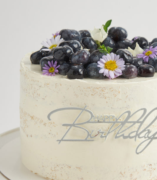Elegant blueberry birthday cake with fresh berries, white buttercream, and Happy Birthday topper