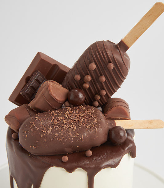 Decadent chocolate layer cake with dark ganache drip, topped with chocolate bar, truffles, and cake pops for birthday