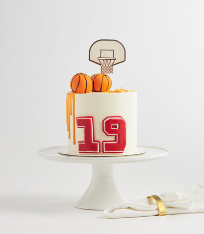 White birthday cake with orange basketball drip, number 19, and miniature basketballs on white stand