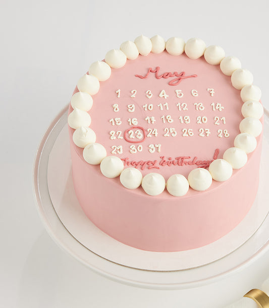 Pink strawberry birthday cake with calendar design and May 23 date circled in icing
