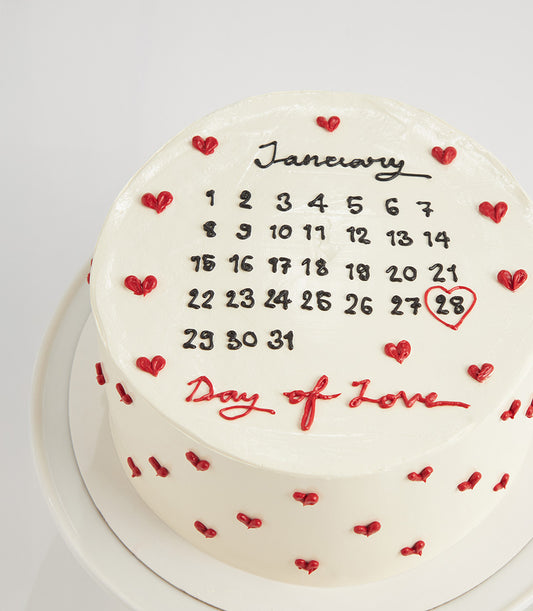 White two-tiered calendar cake with red hearts and "Day of Love" inscription for birthdays
